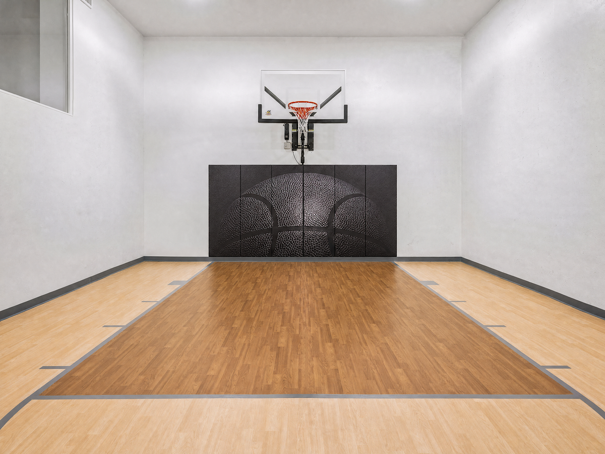 Indoor home basketball court with a wall-mount hoop, black basketball wall padding and Gladiator maple-and-walnut athletic flooring